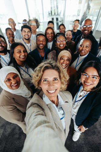 A diverse group of company staff smiling and taking a selfie at the office. Teamwork, unity, and positive corporate culture captured in one shot.